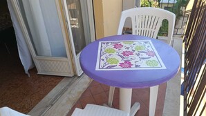 Un petit espace extérieur aménagé en patio, avec une table ronde et deux chaises en plastique blanches.