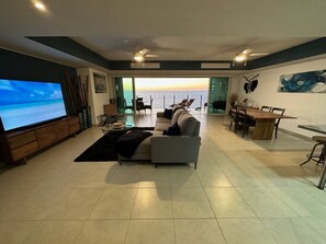 Un soggiorno con una televisione grande, un divano, un'area pranzo e vista sull'oceano.