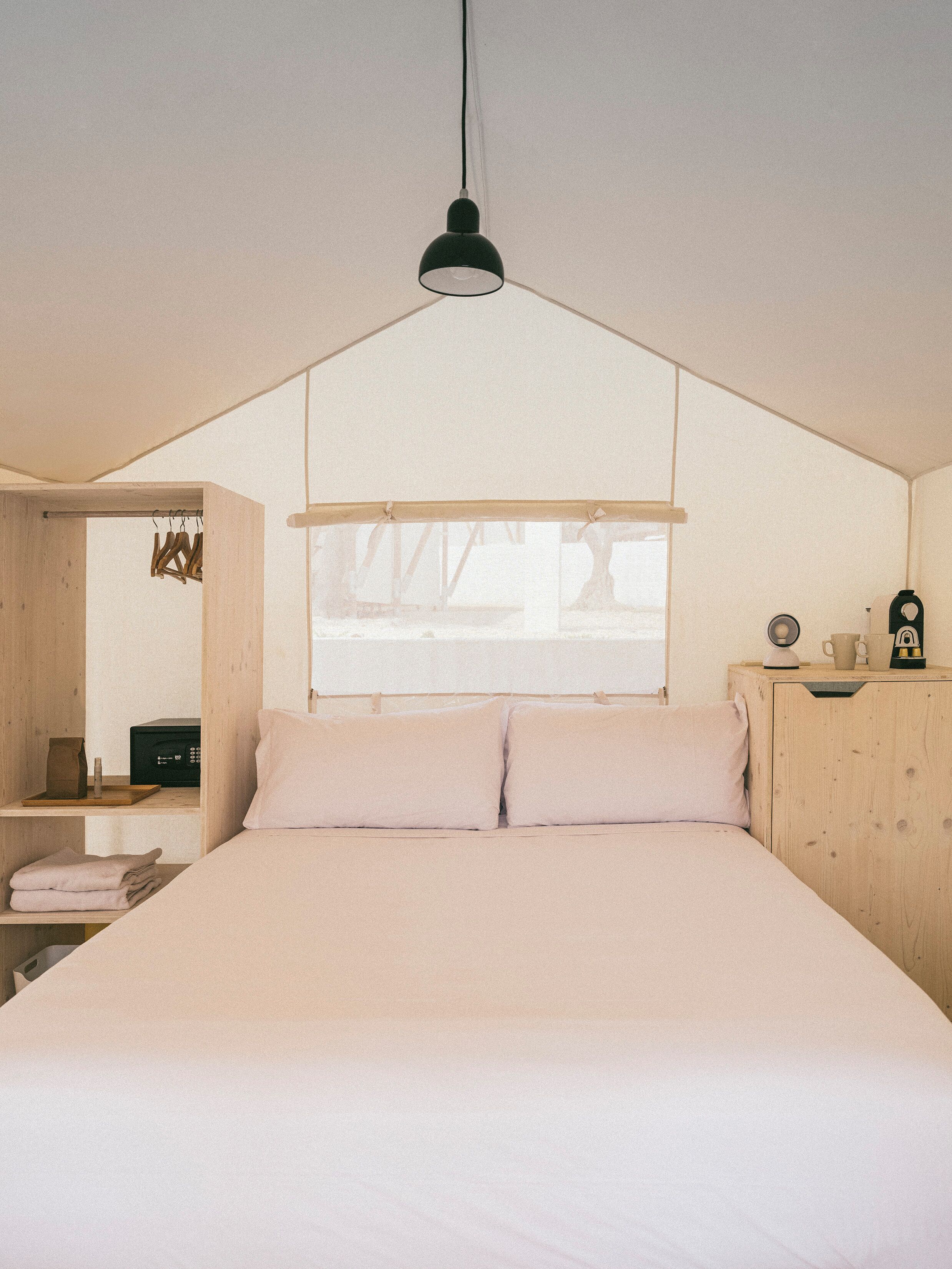 Une chambre à coucher avec un lit, un luminaire suspendu, une fenêtre et une armoire en bois.