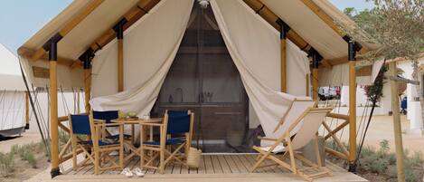 A tented accommodation with a wooden deck, seating area, and a view of the sky.