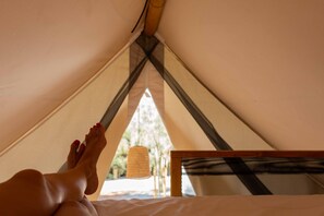 A tent with a bed inside, a hanging light fixture, and a view of the outdoors.