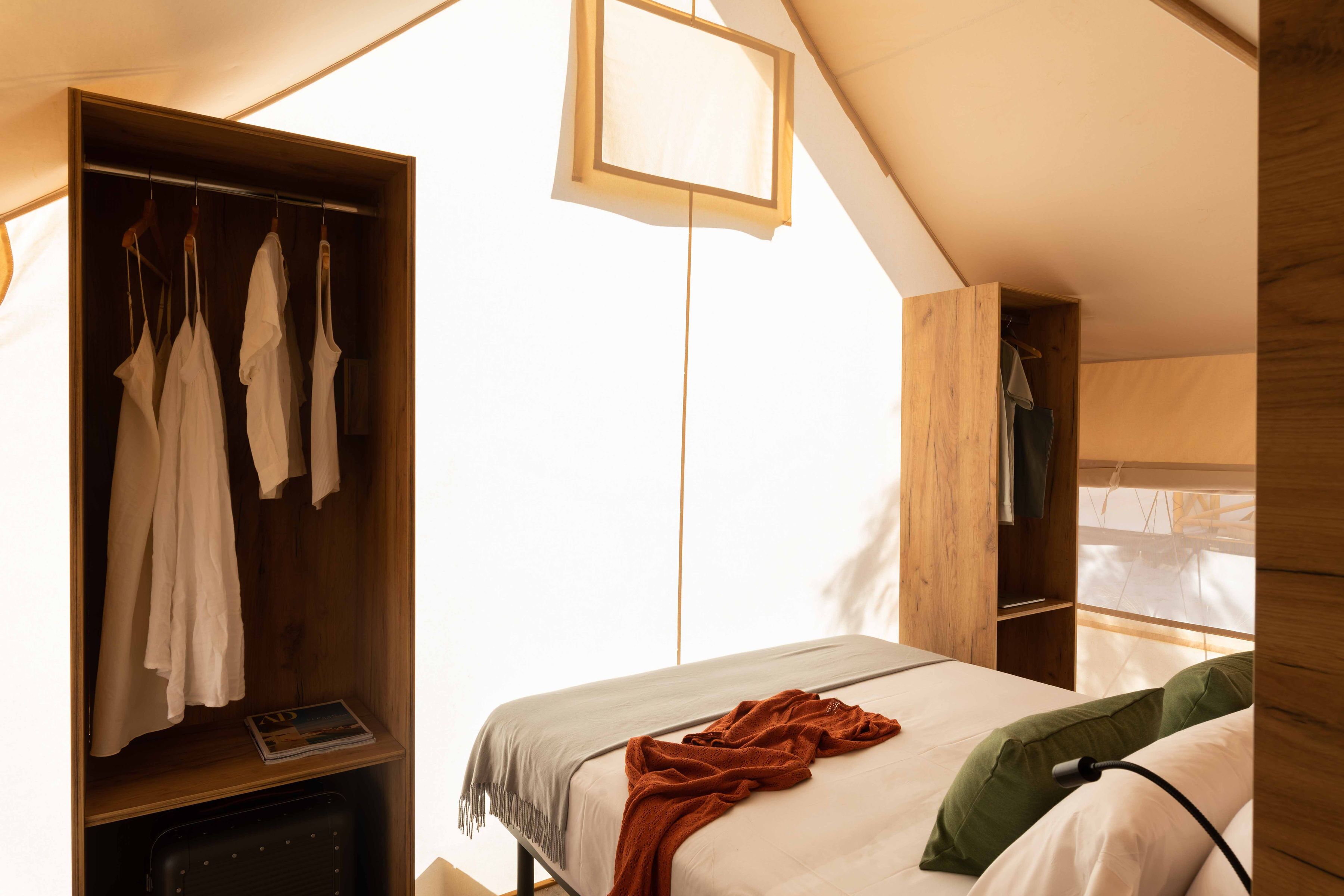 A bedroom with a bed, a wooden wardrobe, and a hanging light fixture.