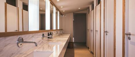 Une longue et étroite salle de bain avec trois lavabos, des lambris en bois et un miroir.