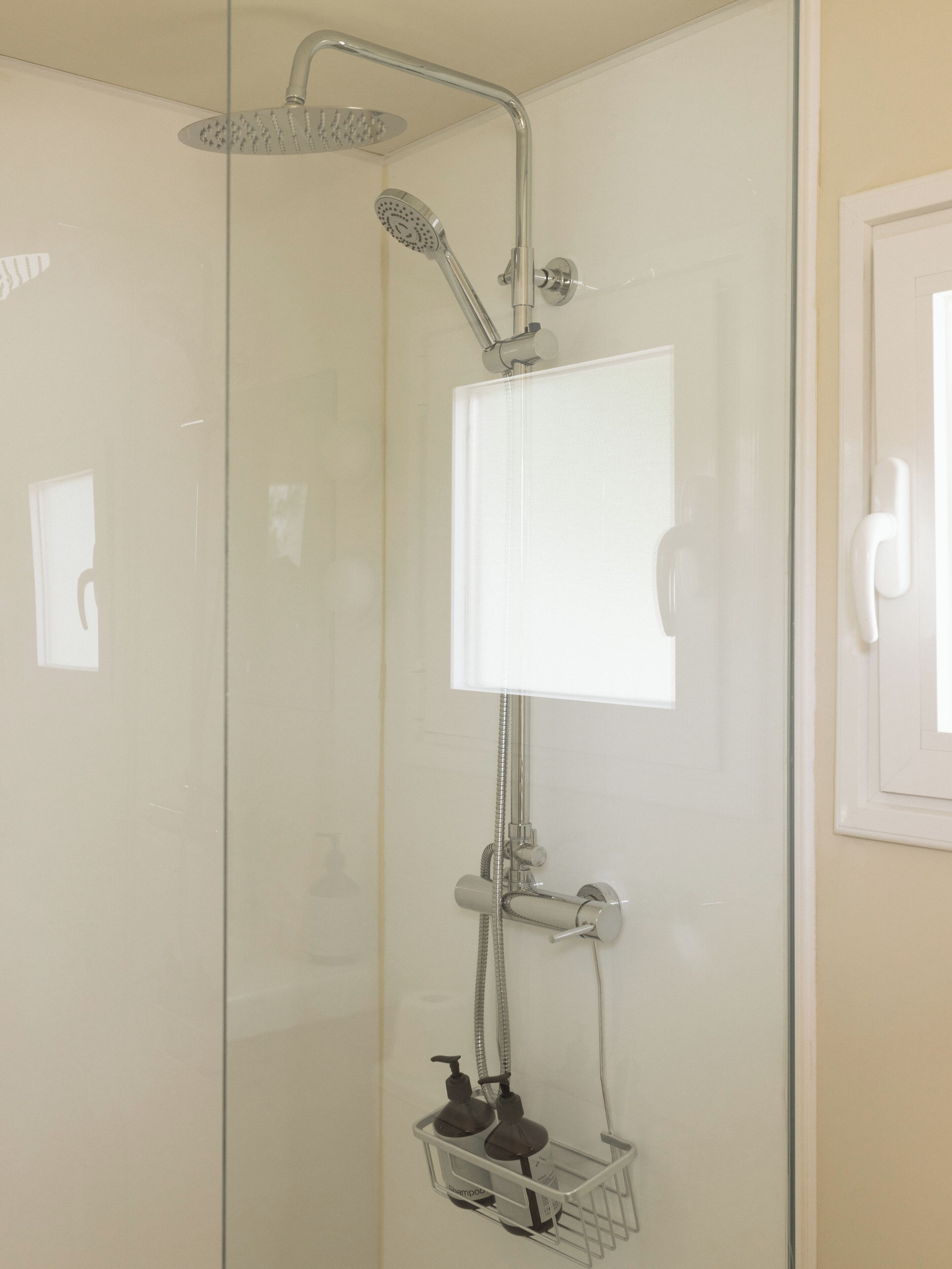 Une douche fermée par des parois en verre, dotée d’un pommeau de douche à main, d’un robinet mural et d’un distributeur de savon.