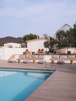 A swimming pool with a wooden deck, outdoor seating, and potted plants.