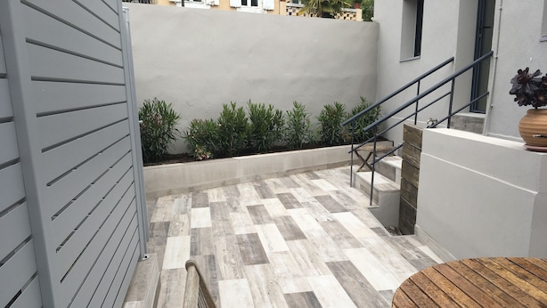 A modern outdoor area with a checkered floor, a wooden bench, a metal staircase, and a potted plant.