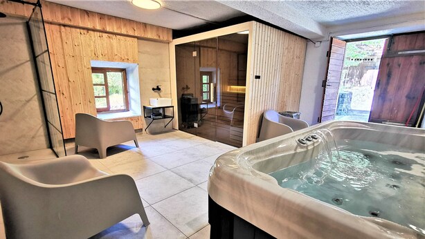 A spa room with a hot tub, two chairs, a window, and a wooden wall.