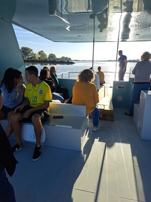 Schiffsausstattung mit Sitzgelegenheiten, Blick auf das Wasser und eine Person, die hinten steht.