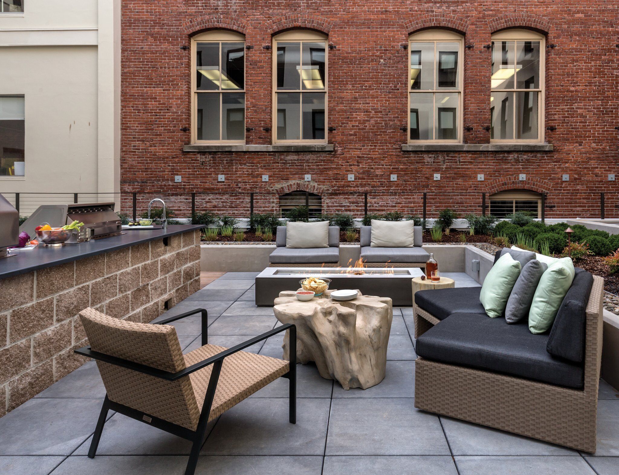 An outdoor patio with a brick wall, a grill, seating area, and a fire pit.