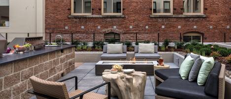An outdoor patio with a brick wall, a grill, seating area, and a fire pit.