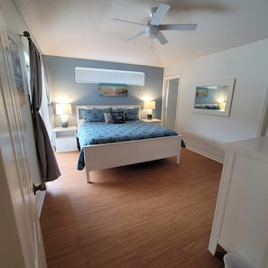 A bedroom with a bed, two bedside tables with lamps, a ceiling fan, a door, and a window with curtains.