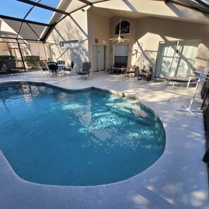 A swimming pool with a curved edge, surrounded by lounge chairs and a covered patio area.