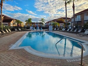 A swimming pool with lounge chairs and palm trees, surrounded by buildings with balconies.