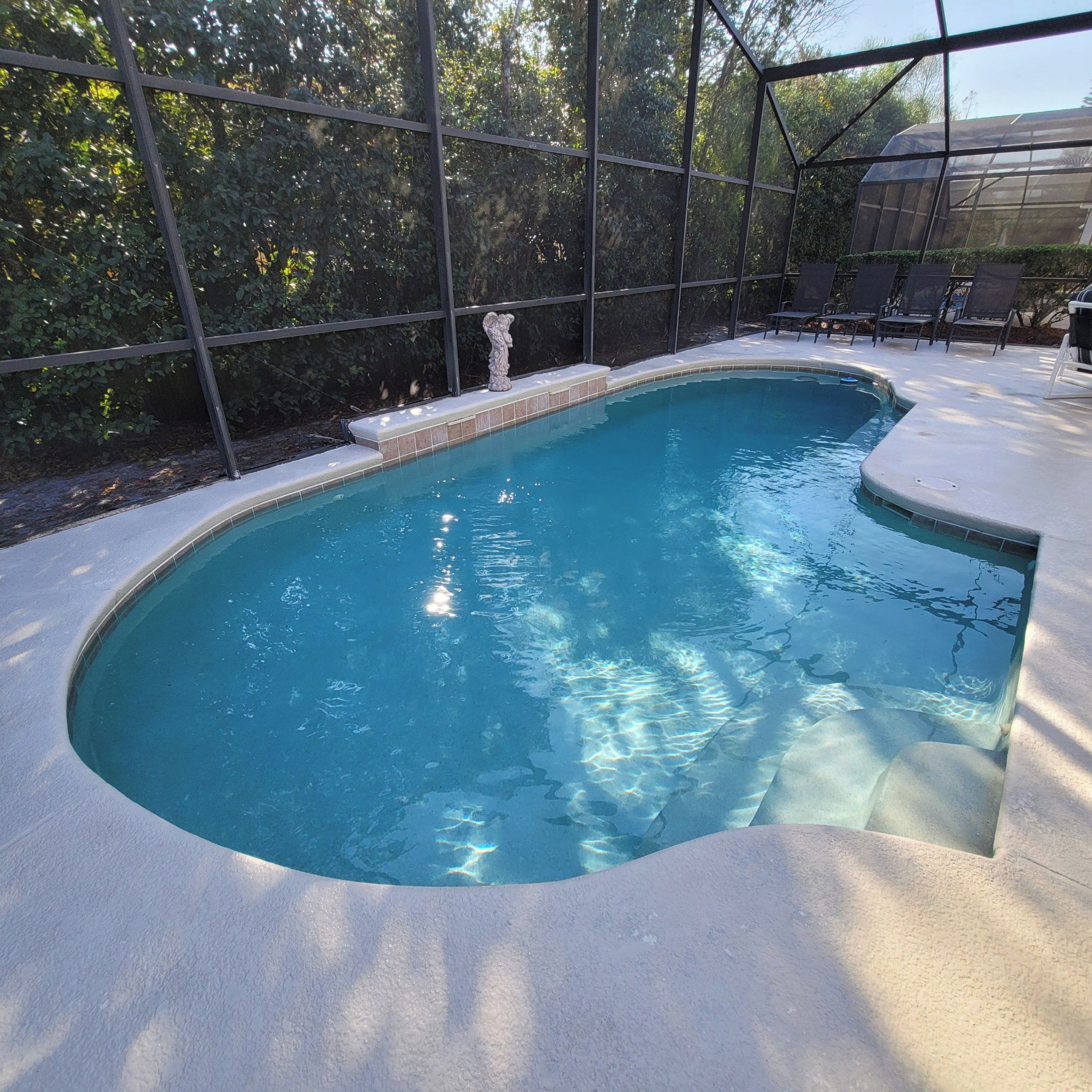 Una piscina con borde curvo, rodeada por una zona techada con sillas y una estatua.
