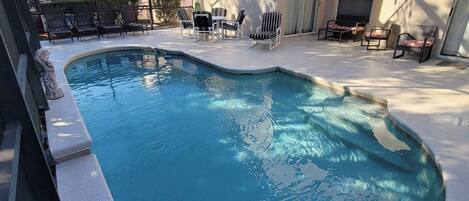 En pool med en böjd kant, omgiven av solstolar och en möblerad uteplats.