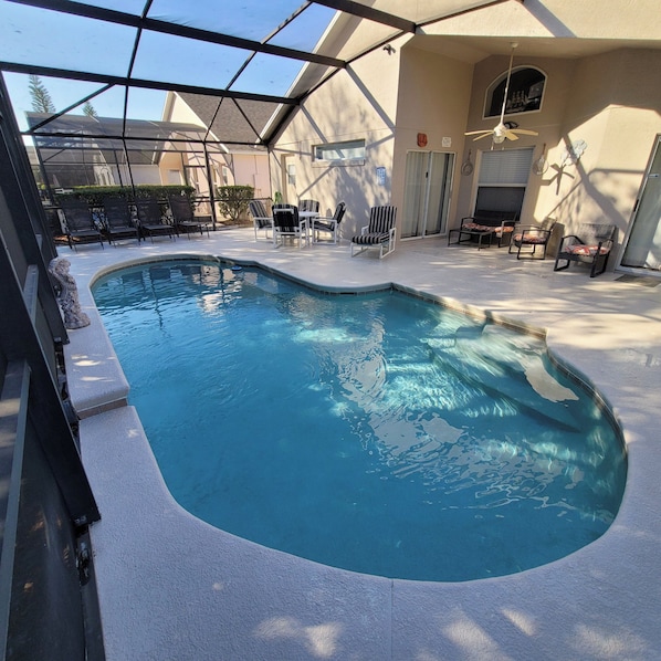 A swimming pool with a curved edge, surrounded by lounge chairs and a covered patio area.