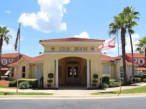 A Club House with a red-tiled roof, a central entrance with a canopy, and palm trees in the background.