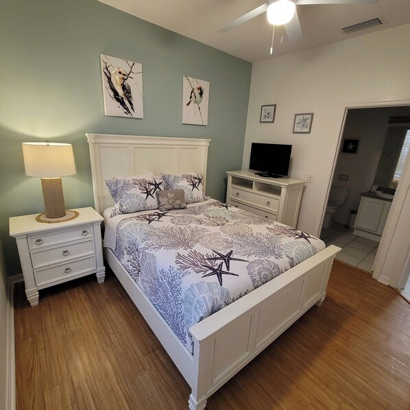 Quarto com cama, mesas de cabeceira, abajur, televisão e obras de arte nas paredes.