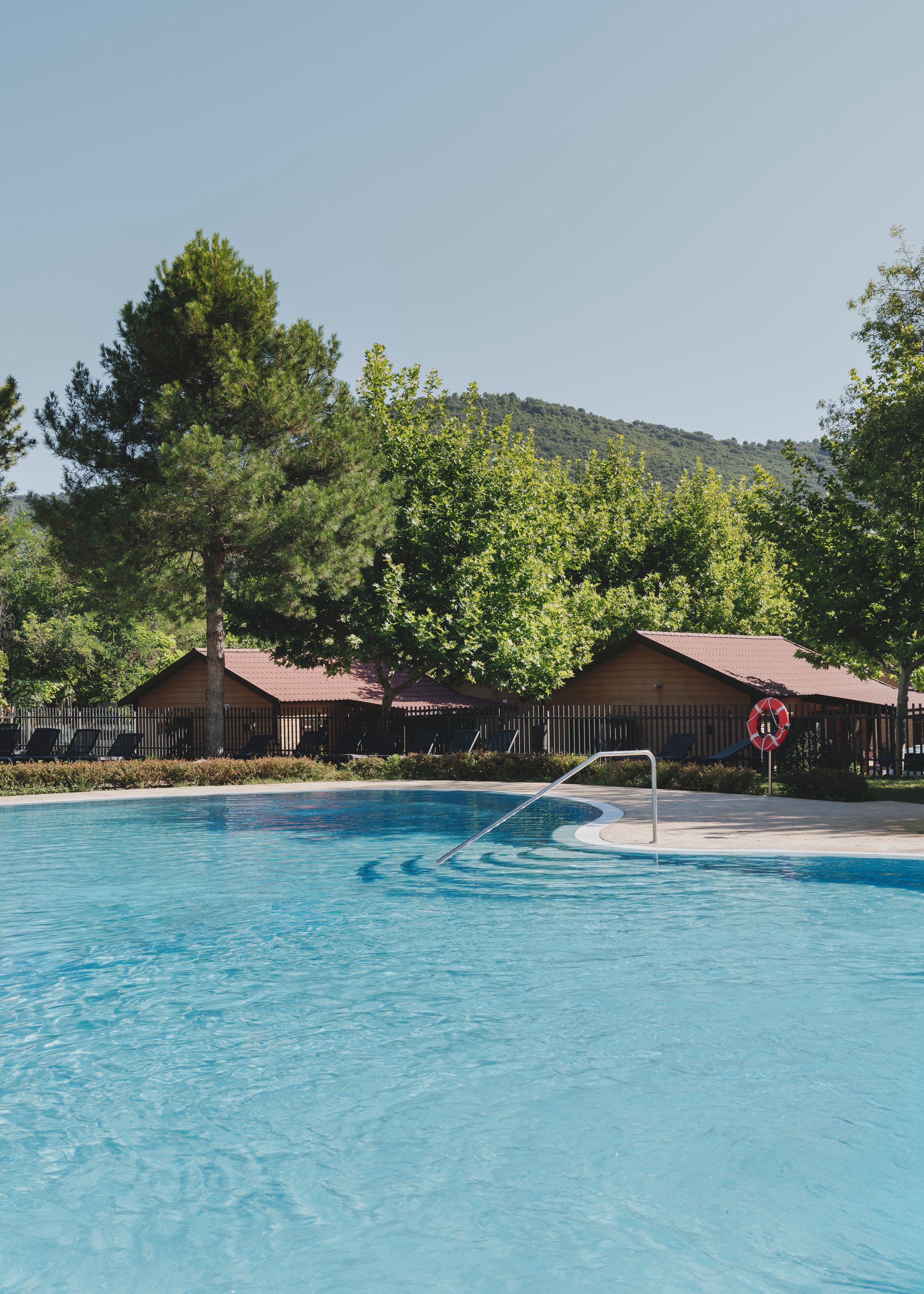 A swimming pool with lounge chairs and a lifeguard chair, surrounded by trees and cabins.