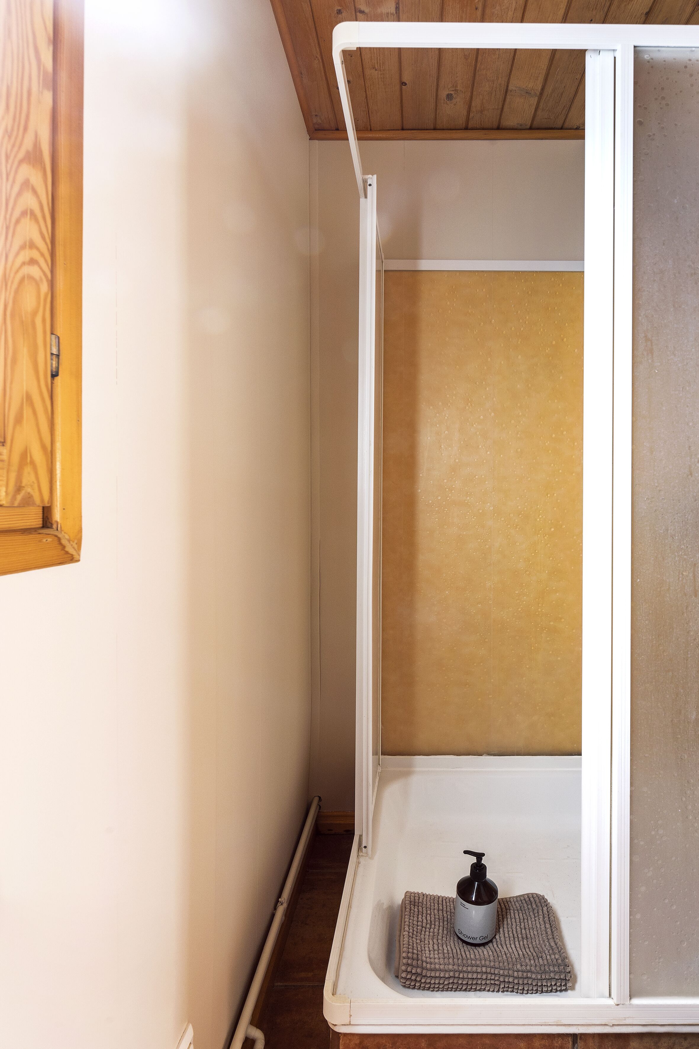 Une petite salle de bain fermée, avec une porte en bois, une serviette et un distributeur de savon posé sur une étagère.