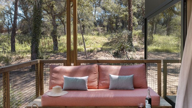 Una terraza de madera con una zona de estar acolchada, una mesita y una cesta.