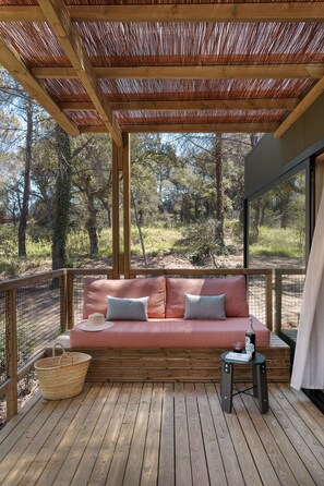A wooden deck with a cushioned seating area, a small table, and a basket. - Wecamp Pirineos (Boltana)