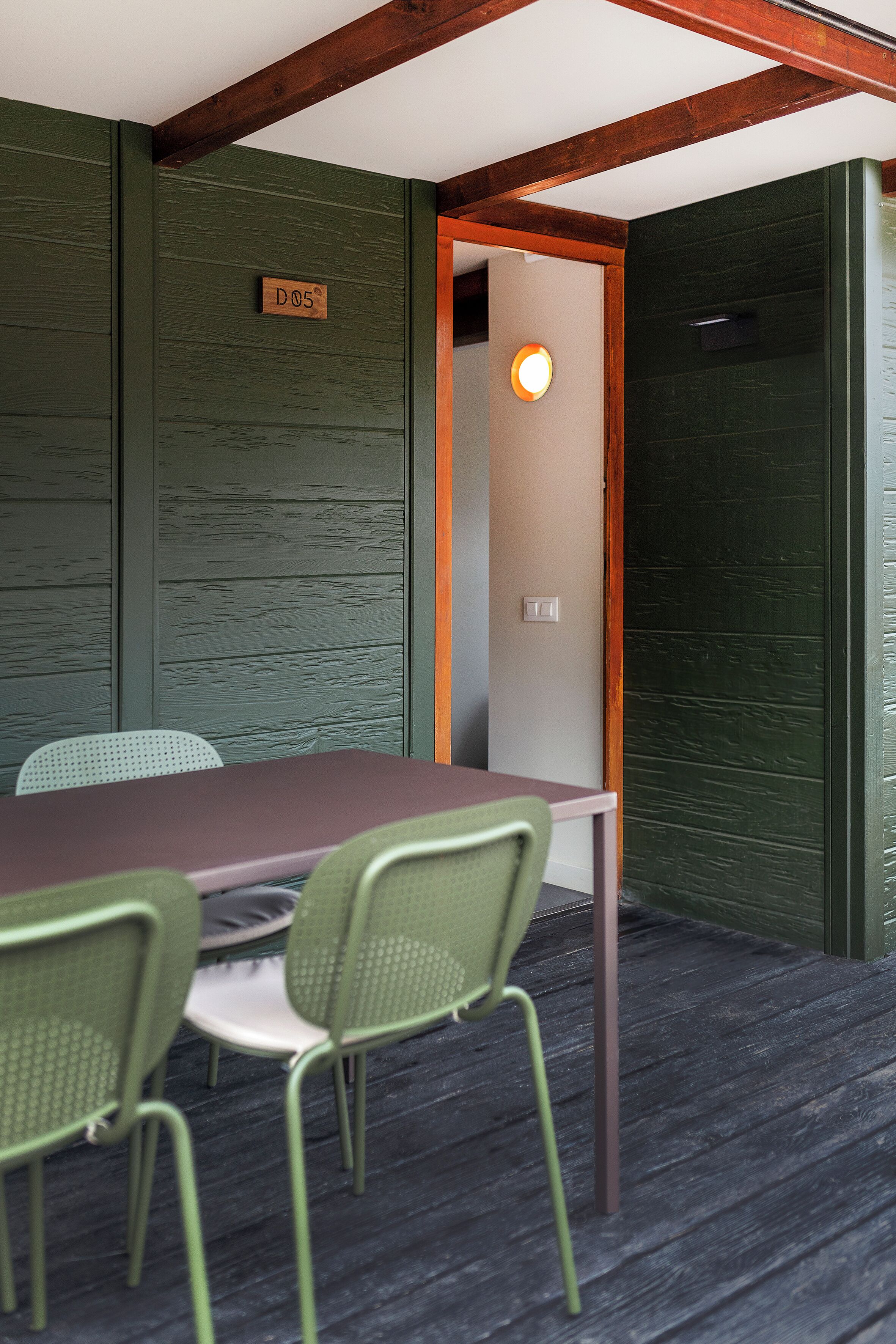 A room with a wooden ceiling, a green wall, a table with chairs, and a door with a sign.