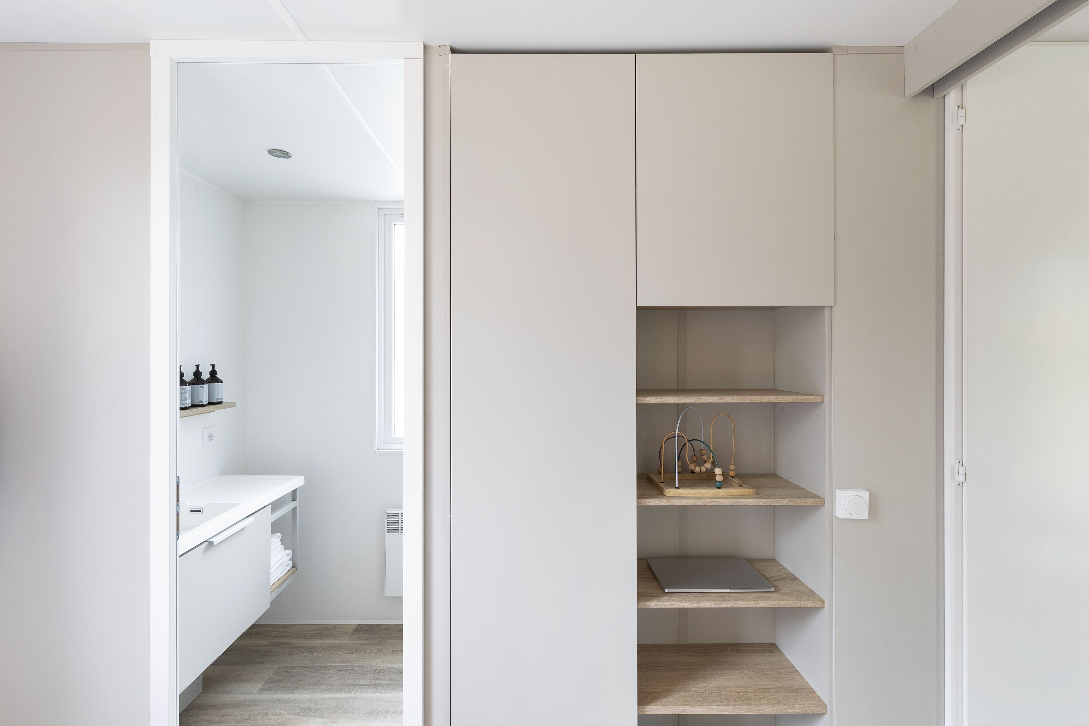 A modern bathroom with a white vanity, shelves, and a shower area.