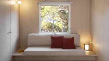 A modern room with a built-in bench, a window with a view of trees, and a bedside table with a lamp.