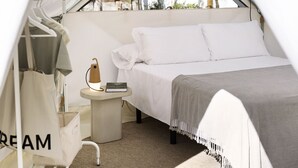 Una habitación con tienda de campaña, una cama, una mesita con lámpara y un bolso colgado que dice 'CREAM'.