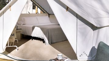Een tent met een bed erin, een klein tafeltje met een kopje en een boek, en een stoel.