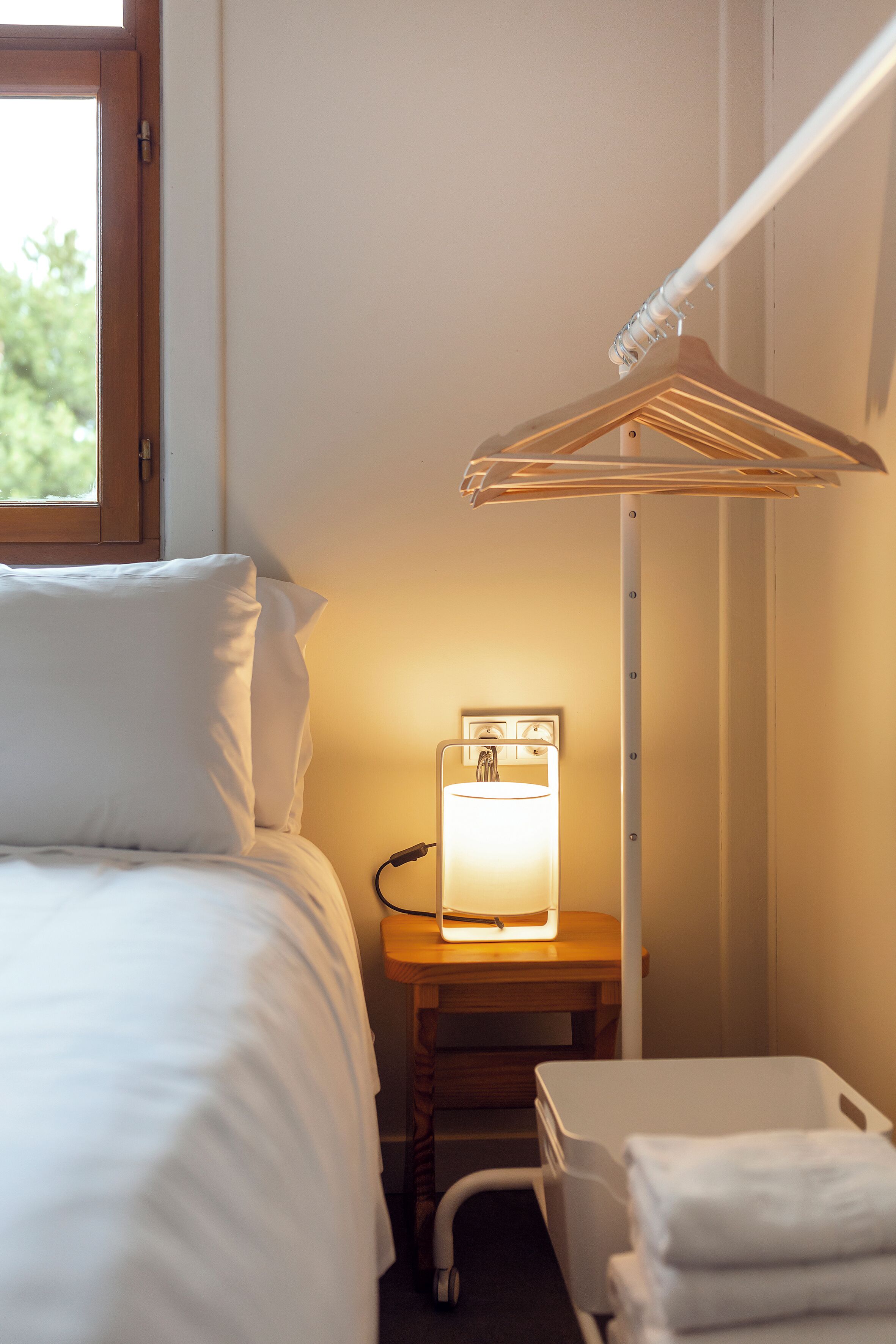 A hotel room with a bed, bedside table, lamp, and a hanging clothes rack.