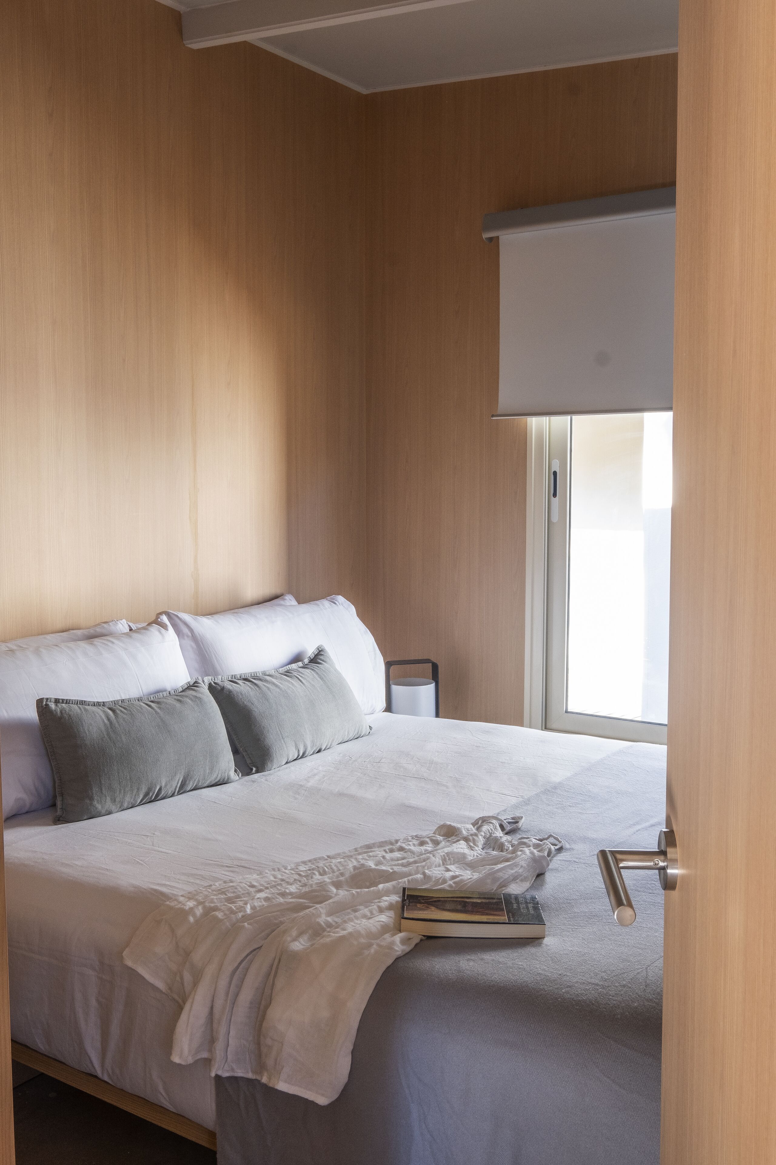 Una cama bien hecha con almohadas, una mesita de noche y una ventana con persianas.