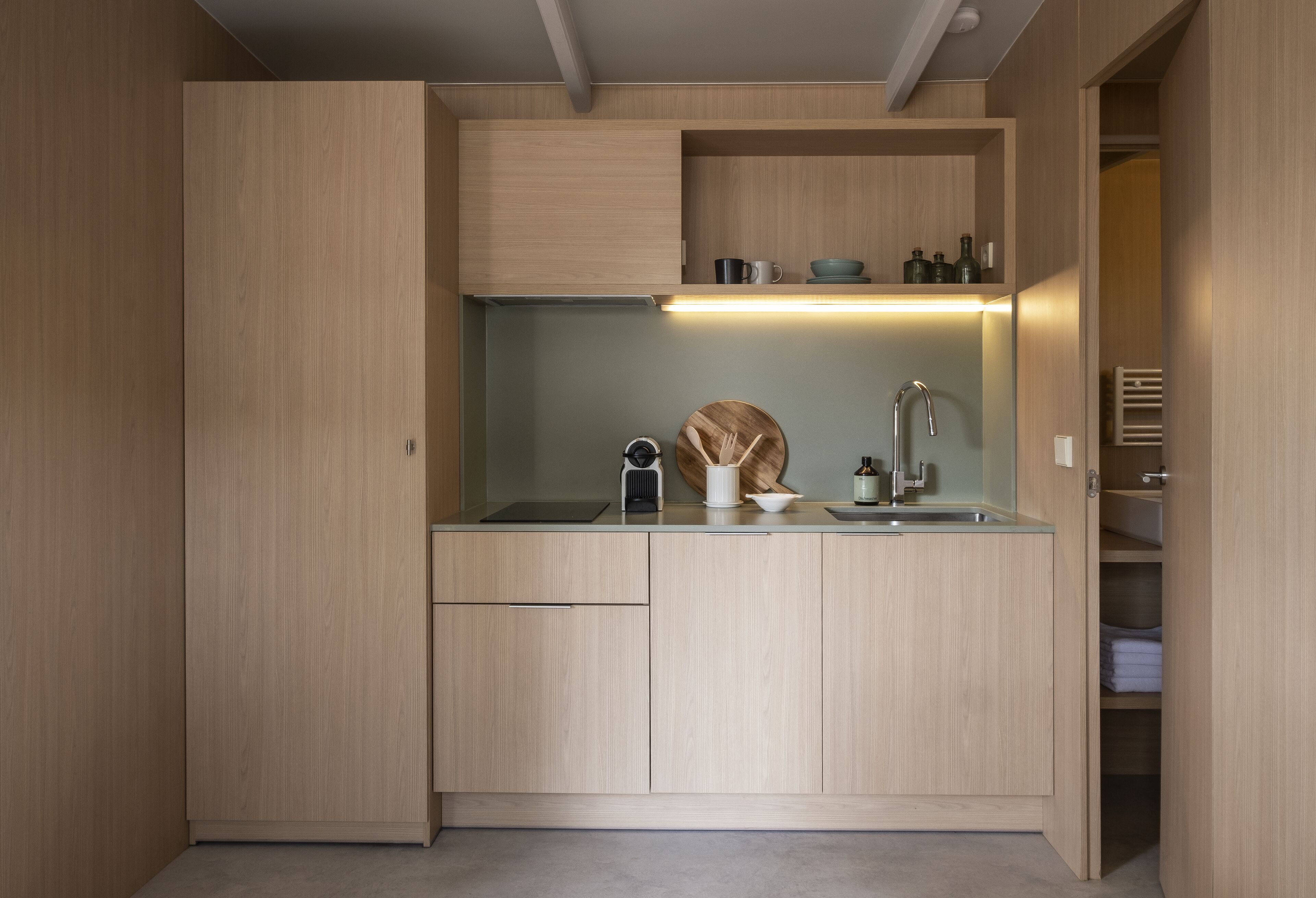 A compact kitchen with wooden cabinetry, a built-in sink, and a countertop with a kettle and a bottle.