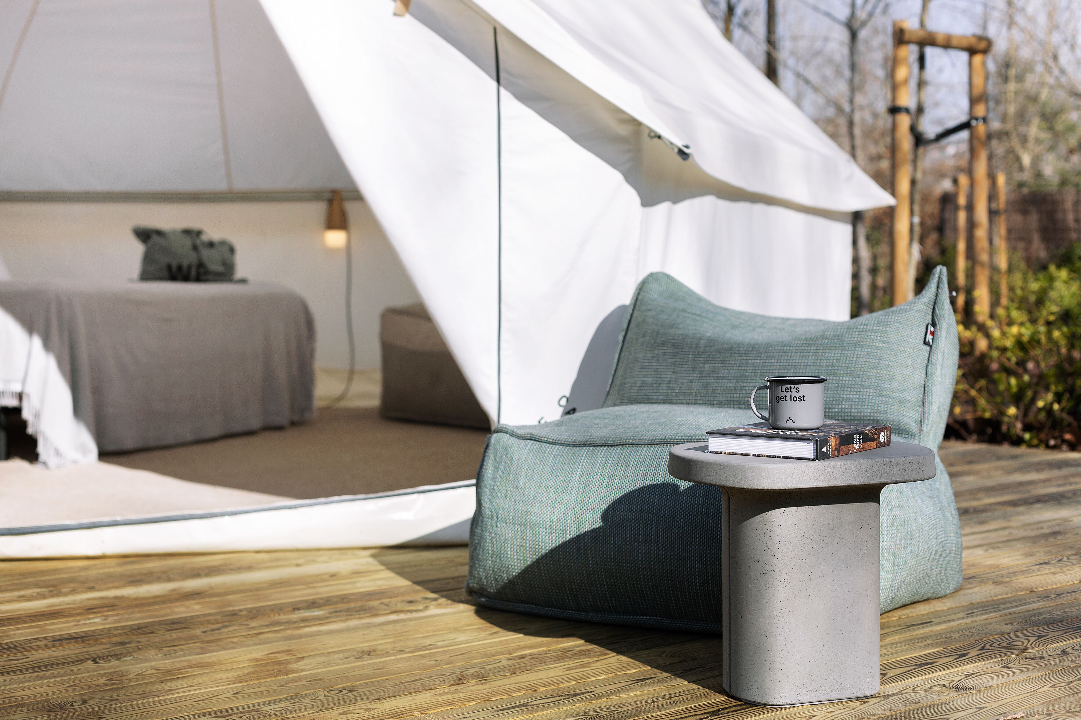 Een gezellig buiten zitgedeelte met een zachte stoel en een kleine tafel, een tent op de achtergrond, en een houten terras.