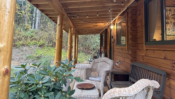 Una cabana de fusta amb un porxo cobert, mobles de vimetla i vistes al bosc circumdant.