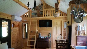 Interior acollidor d'una cabana amb un dormitori a la biga, zona de menjador i cuina.