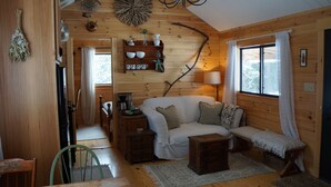 Interior acollidor d'una cabana amb elements de fusta, un sofà blanc, una banca i una zona de dinar amb taula i cadires.