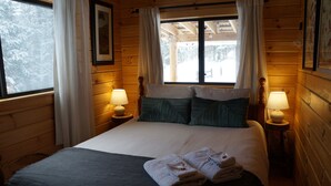 Habitació de cabana de fusta amb un llit, dues làmpades de nit i una finestra amb cortines.