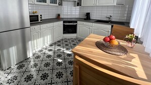 Una cocina moderna con armarios blancos, un microondas, un horno y un lavamanos. Hay una mesa de comedor con un mantel individual y fruta.