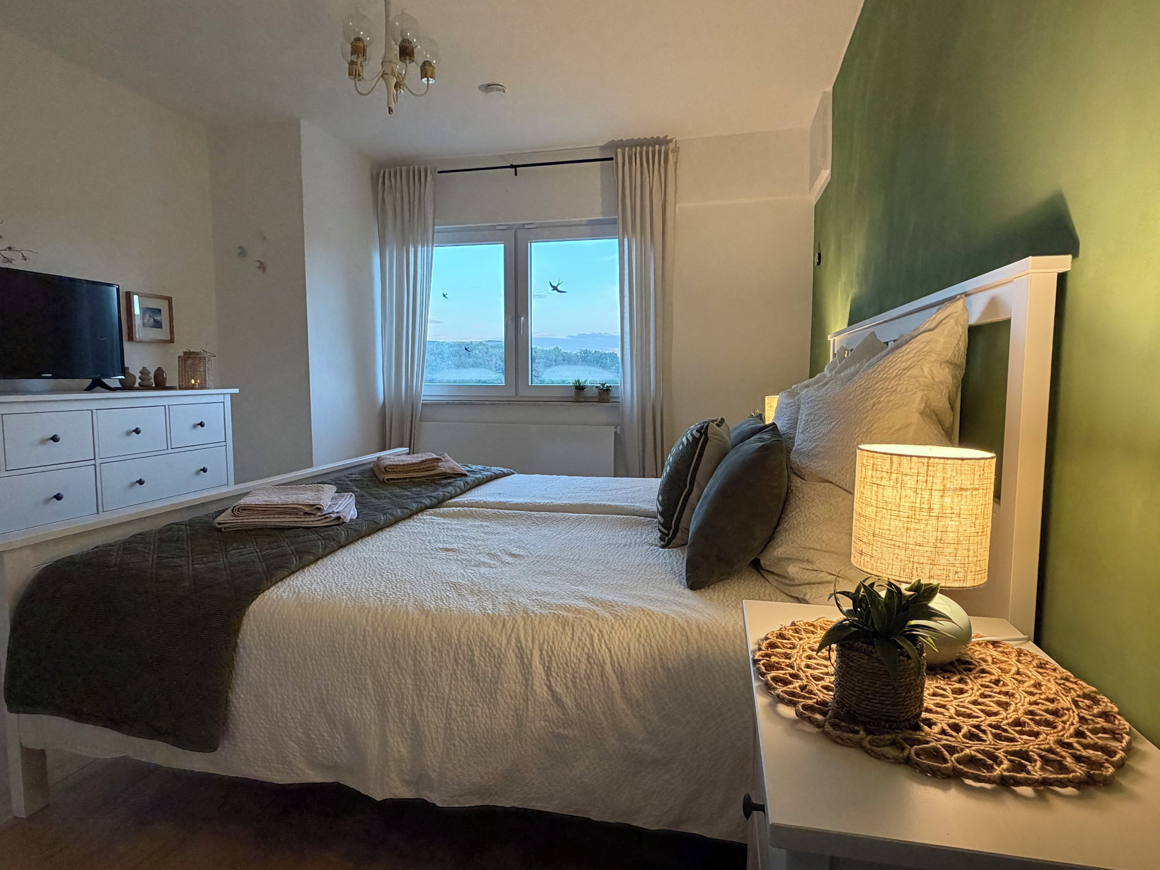 Une chambre à coucher avec un lit, une lampe de chevet, un téléviseur et une fenêtre avec des rideaux.