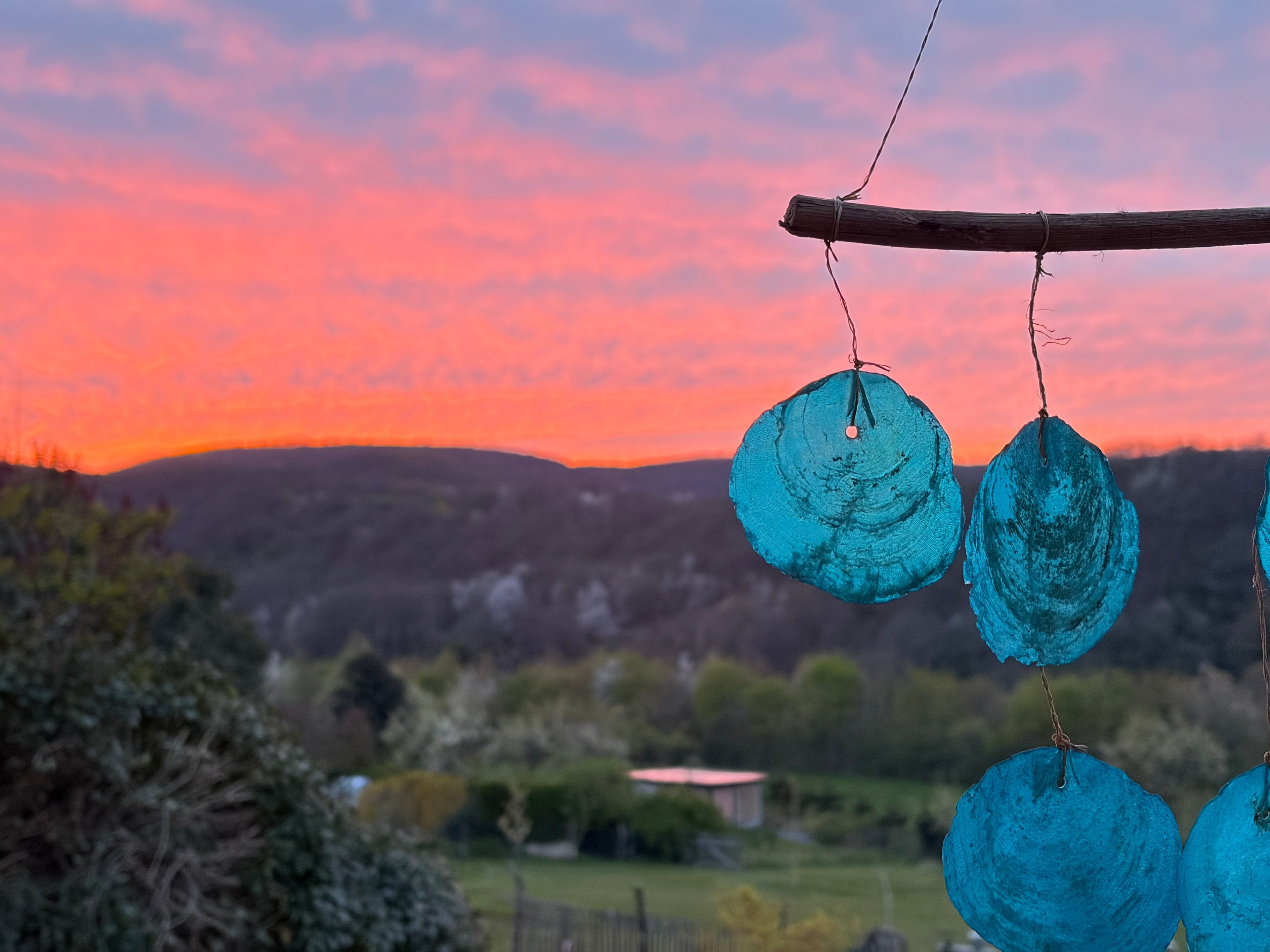 Een uitzicht op een landelijk landschap bij zonsondergang, met een houten constructie met daaraan hangende objecten.