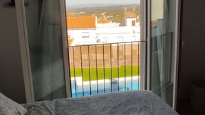 A bedroom with a patterned bedspread, a sliding glass door leading to a balcony with a pool view. - Casa Rural con Chimenea en Dormitorio, y Sala de Juegos. Con Piscina en Verano!! (Segura de León)
