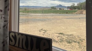 Une fenêtre donnant sur un paysage rural, une enseigne en bois portant le mot « sourire », et un rideau partiellement visible.