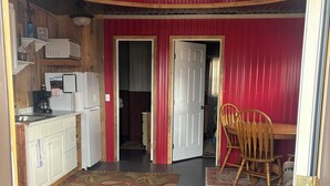 Une cuisine compacte avec des meubles blancs, un réfrigérateur et un four à micro-ondes. On y trouve également un coin repas avec une table et des chaises en bois.