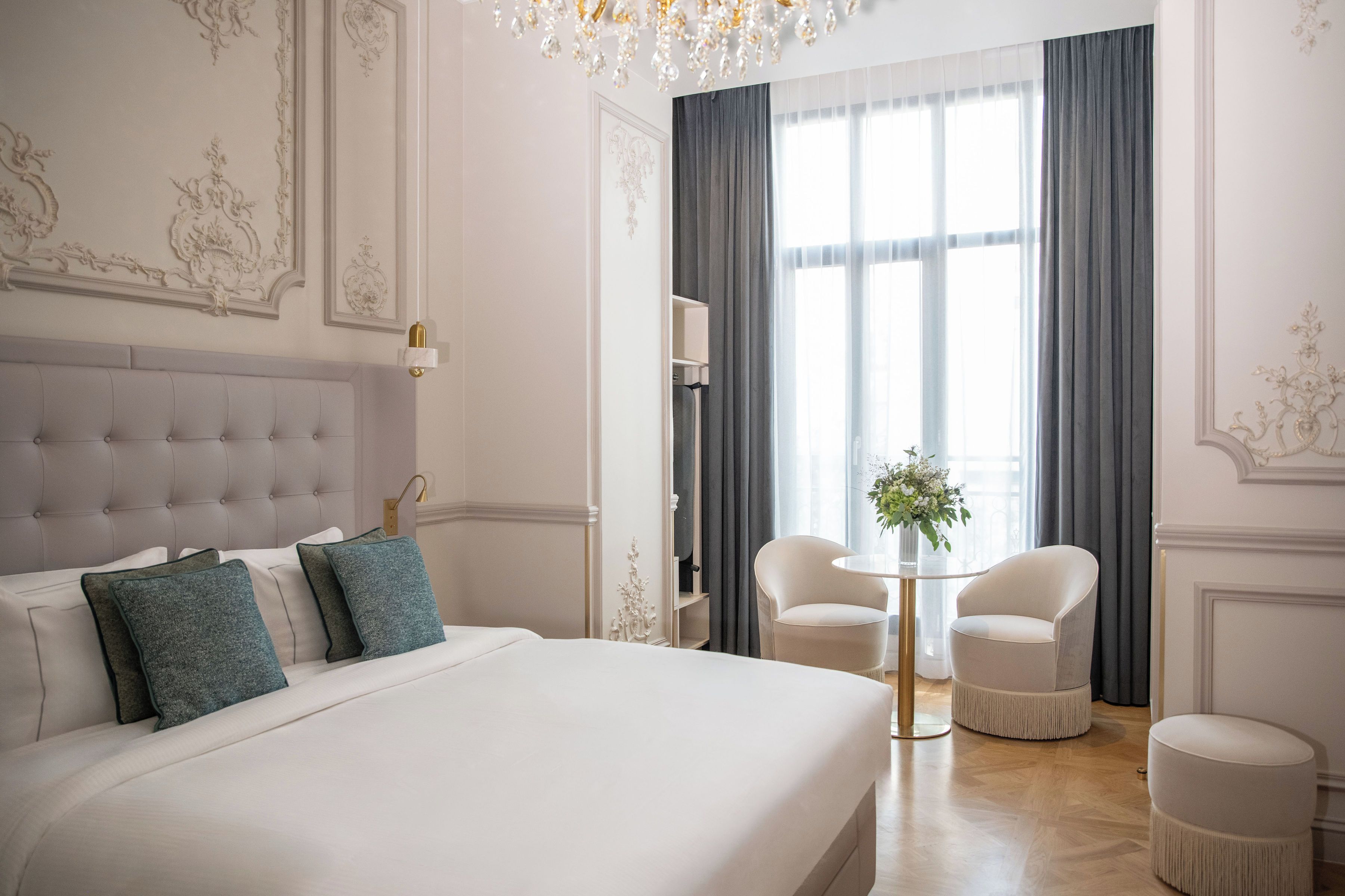 A hotel room with a large bed, a chandelier, a small table with a vase, and two chairs.