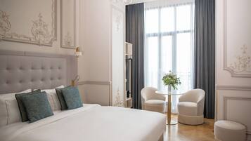 A hotel room with a large bed, a chandelier, a small table with a vase, and two chairs.