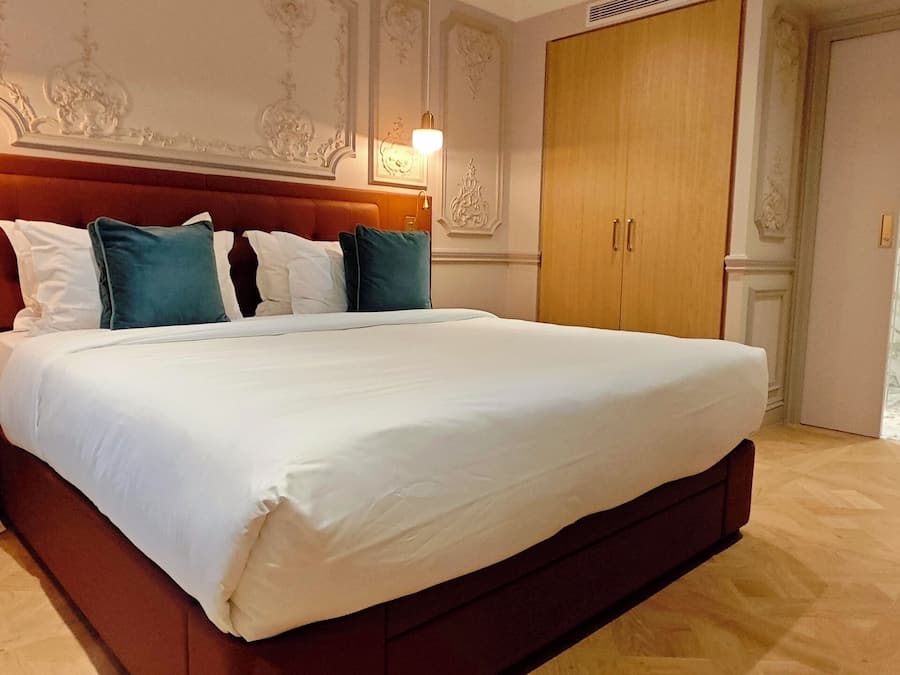 A hotel room with a large bed, a nightstand, a chair, and a wardrobe.