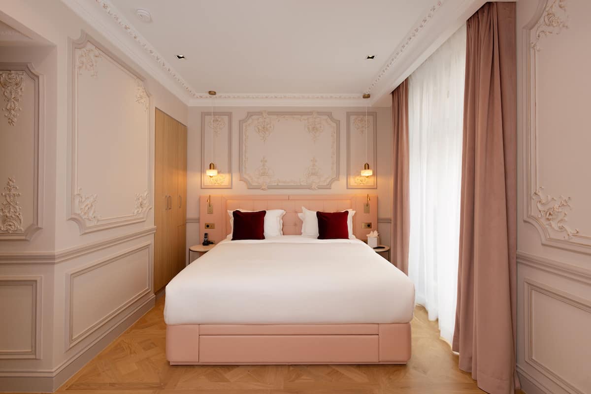 A spacious bedroom with a large bed, ornate wall paneling, and a classic chandelier.