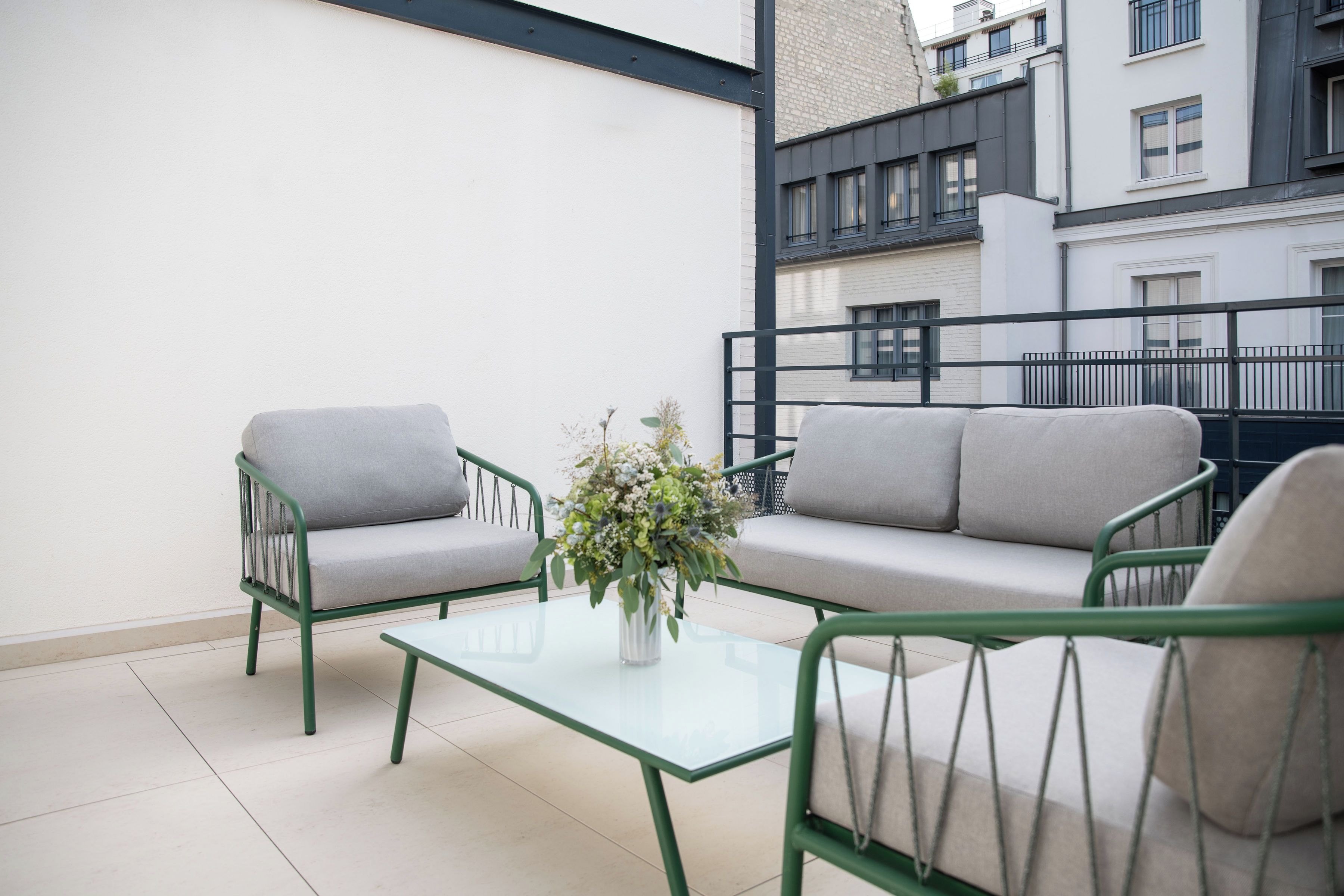 Un balcon avec deux canapés gris, une table en verre et un vase rempli de fleurs.